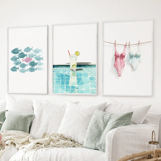 Fun coastal wall art set of 3 watercolor prints featuring a lemonade by the pool, a school of fish, and pastel swimsuits. White frames for living room.