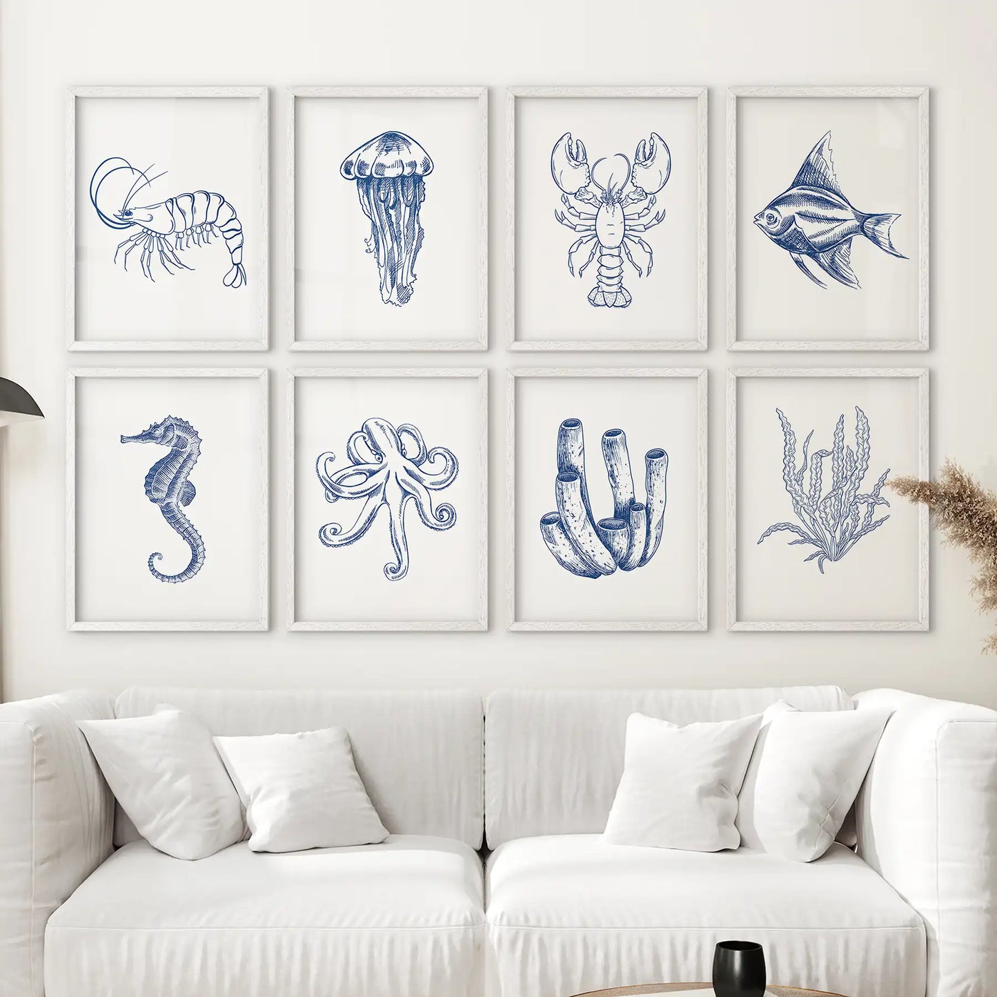 Nautical sea life art set shrimp, seahorse, angelfish, and more in a blue and white coastal themed gallery wall. White frames above the sofa.