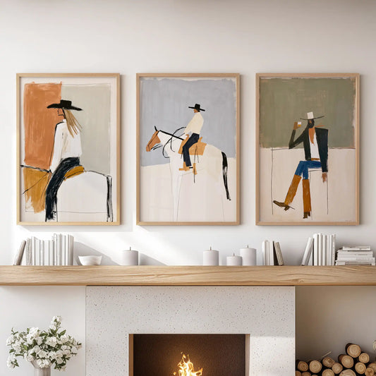 Three framed abstract cowboy-themed art prints are displayed side-by-side in a mockup of a living room above a fireplace mantel with candles and books.