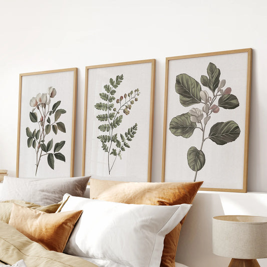 Neutral floral prints, a three-piece wall art set in solid oak frames, spans the bedroom wall over the headboard, layering in warm, understated botanicals.