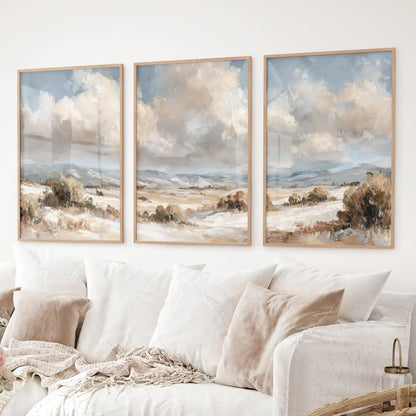 Set of 3 landscape prints in warm neutral tones with mountains and cloudy skies. Thinwood frames over the couch.