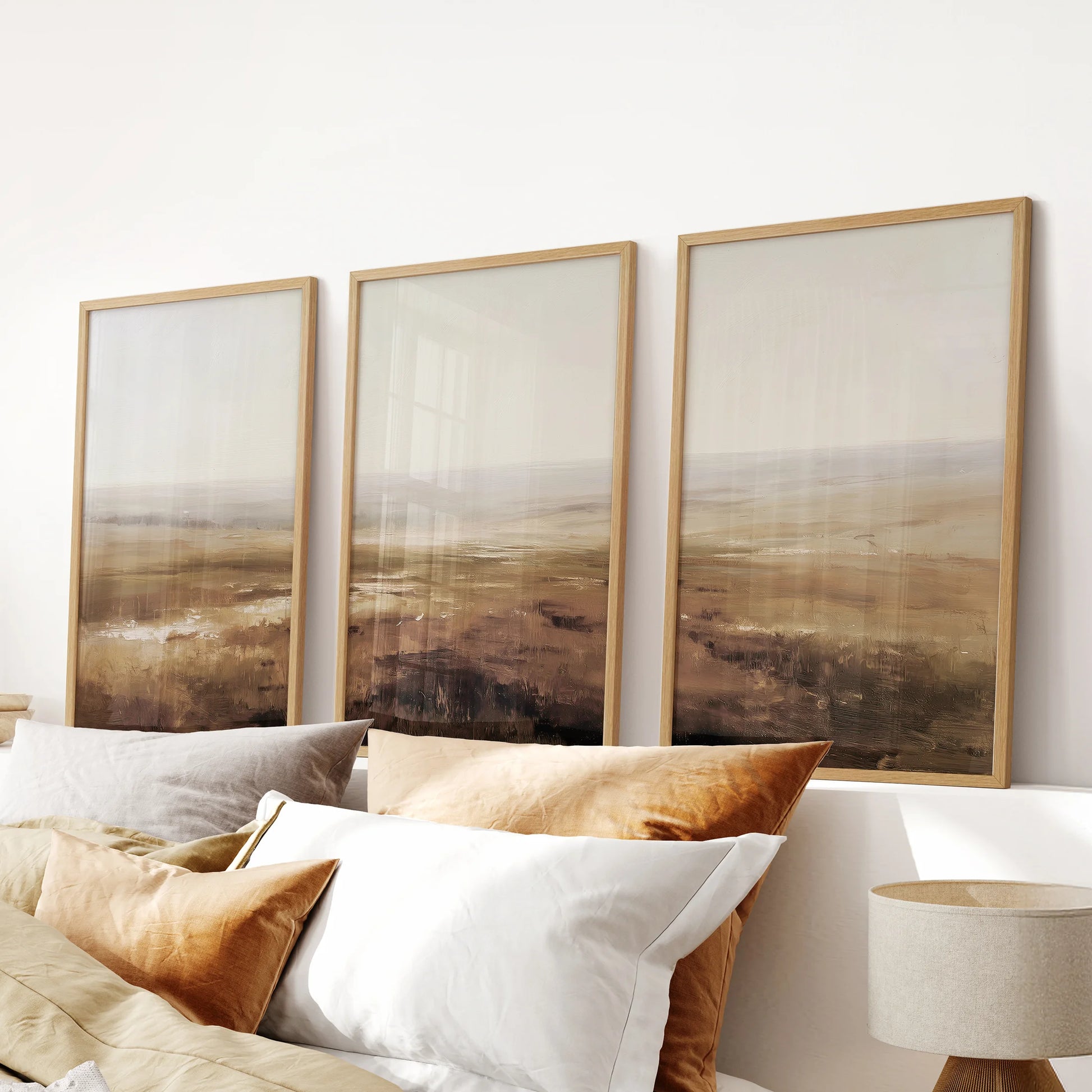 Three-piece abstract landscape artwork in warm wooden frames, featuring earthy tones that center the space above a bedroom headboard.