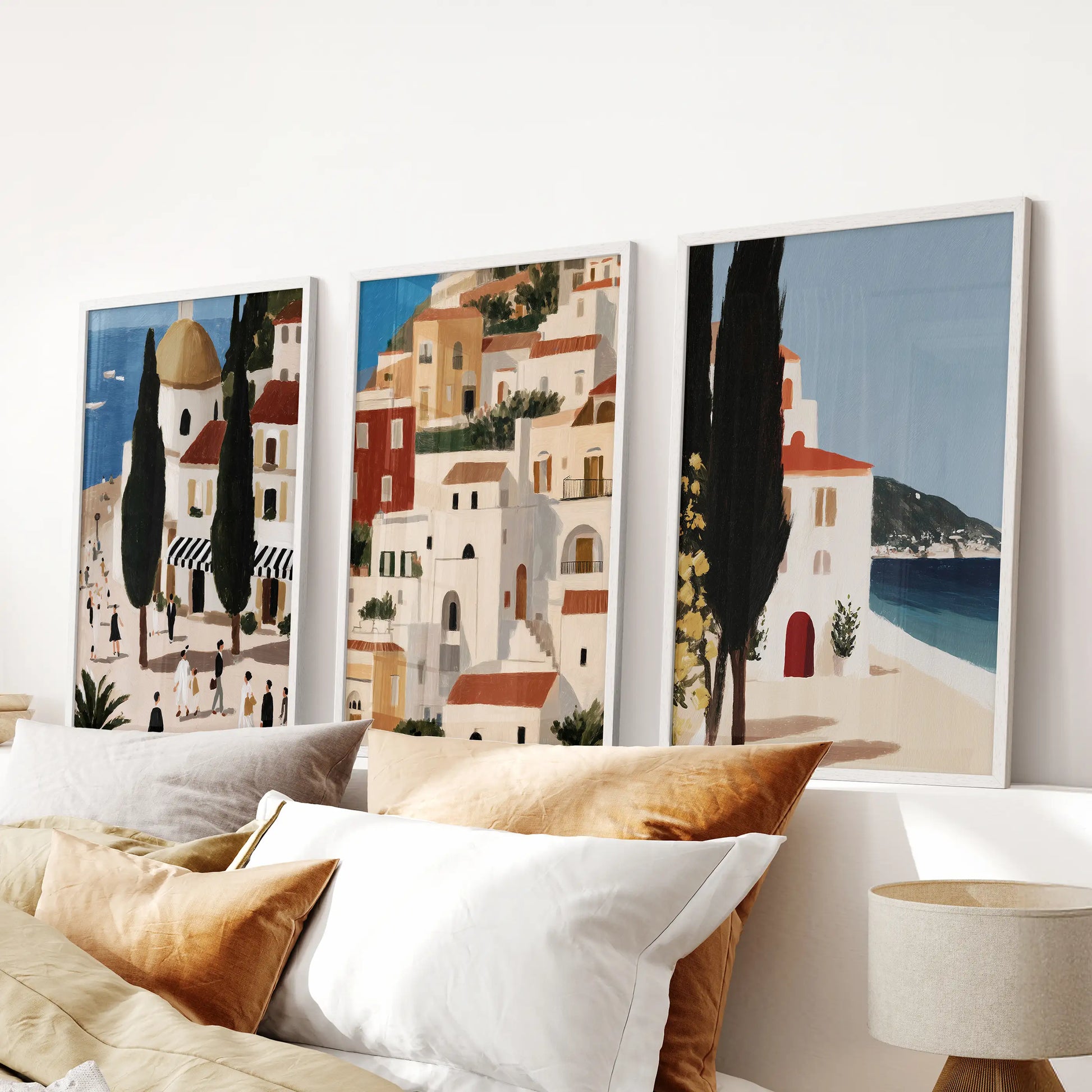Set of three Andalusia travel prints in white frames spans the headboard wall, adding airy architecture and coastal color to the bedroom.