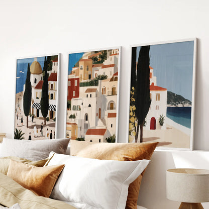 Set of three Andalusia travel prints in white frames spans the headboard wall, adding airy architecture and coastal color to the bedroom.