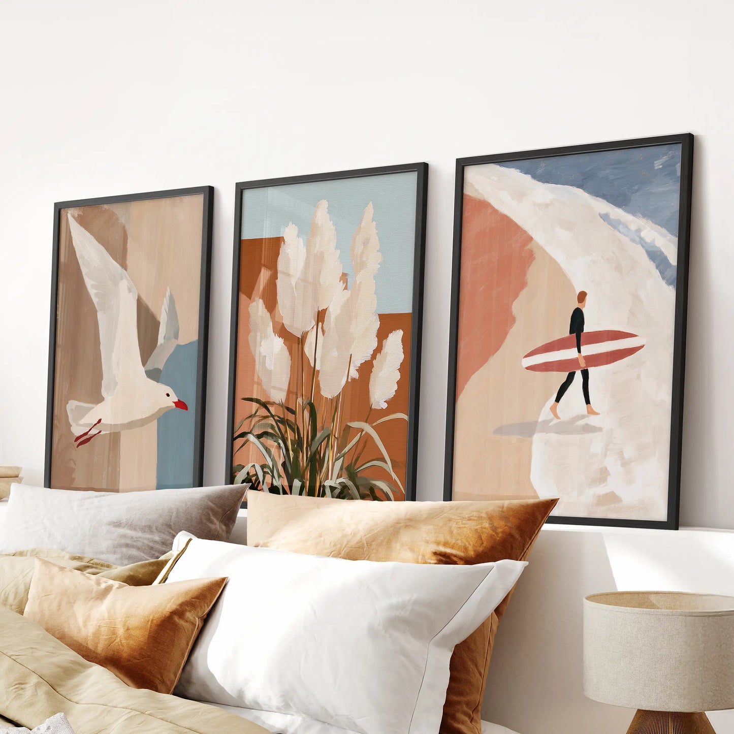 Three black-framed wall prints of pampas grass near dunes sit above the bed headboard, adding soft texture and a restful beach spirit to the bedroom.
