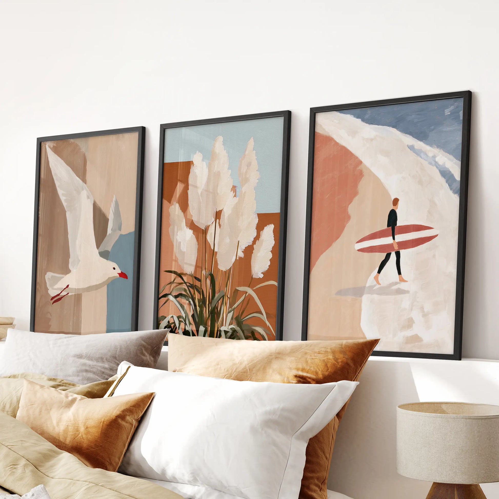 Three black-framed wall prints of pampas grass near dunes sit above the bed headboard, adding soft texture and a restful beach spirit to the bedroom.