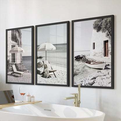 A 3-print wall art bundle shows beach umbrellas on a Greek shore in slim black frames. Displayed above the bath, it adds a calm coastal feel to the bathroom.