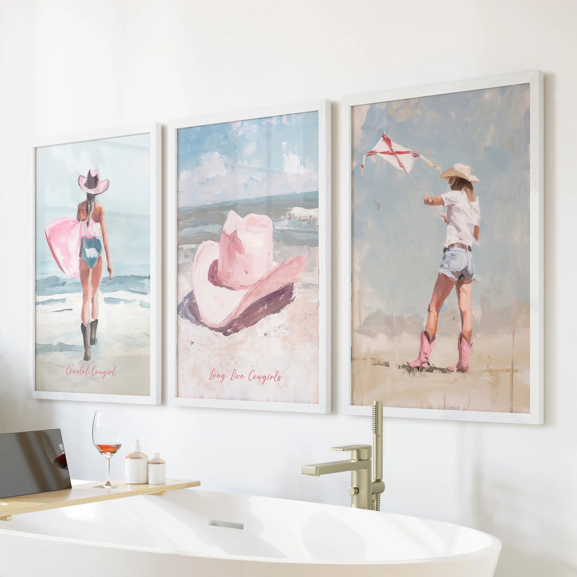 A 3-print white-framed wall art set pairs vintage western flair with coastal pink tones, floating above the bathtub for a calm, sunlit finish.