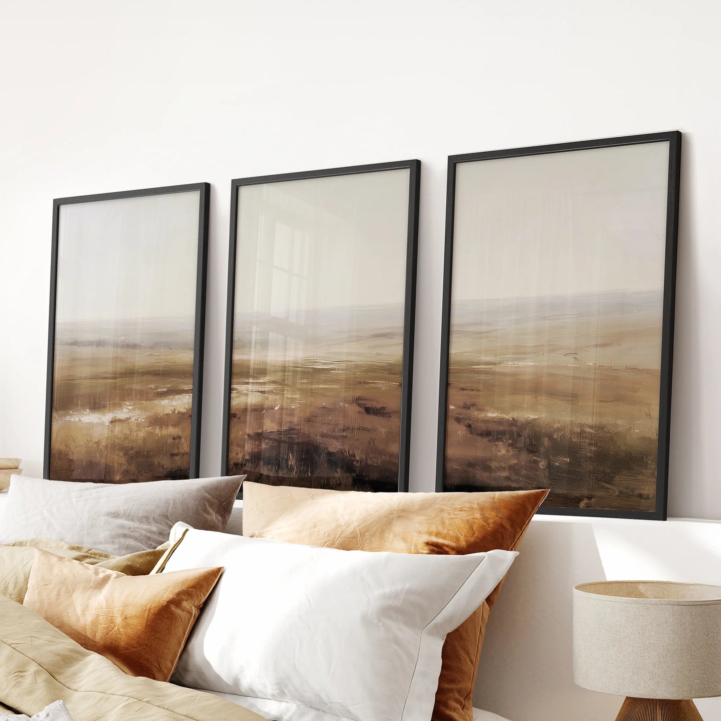 Three-piece abstract landscape wall art in beige and brown tones, framed in black and styled neatly above a bed for a serene bedroom look.