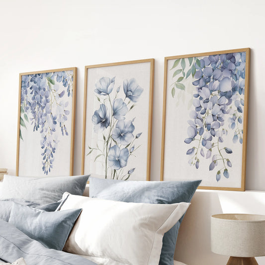 Light blue botanical sprigs, a large set of three oak-framed wall art prints, align above the headboard to ground a blue bedroom in soft botanical color.