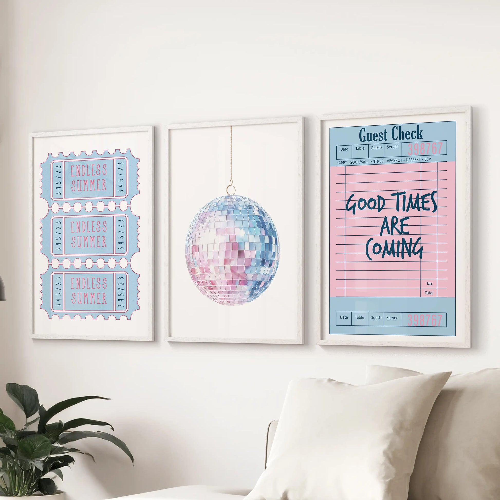 A trio of white-framed wall prints with disco ball, guest check, and beach ticket motives brightens the living room with soft pink-and-blue coastal charm.