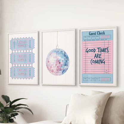 A trio of white-framed wall prints with disco ball, guest check, and beach ticket motives brightens the living room with soft pink-and-blue coastal charm.