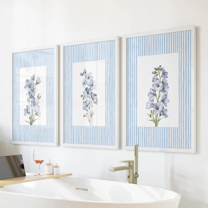Blue watercolor wildflowers set of 3 wall posters in white frames, displayed above a freestanding tub in a bathroom.