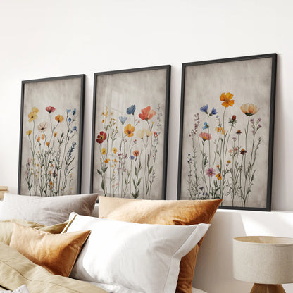 Vintage flower paintings in a set of three framed wall art prints, black edged and composed to sit neatly over the headboard in a relaxed bedroom.