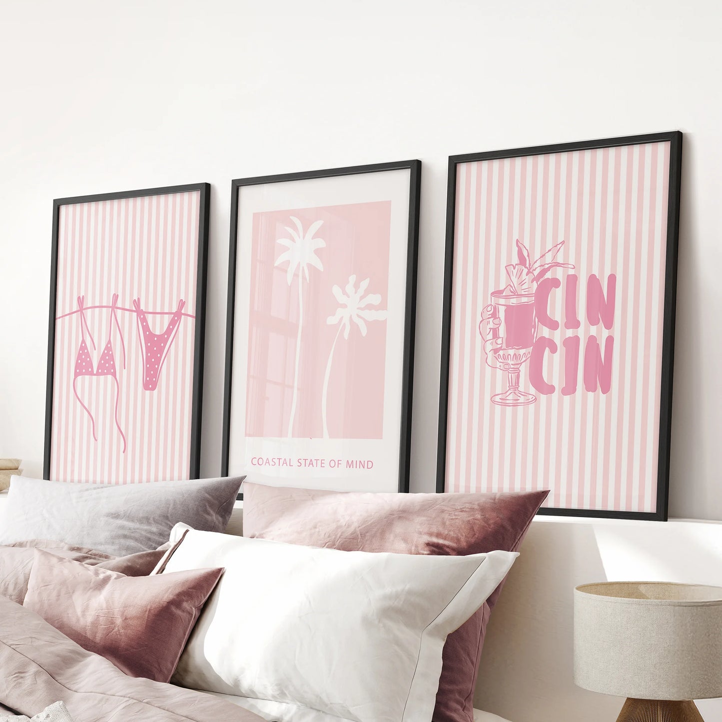 Palm trees and shoreline wall art, a trio in sleek black frames, hangs above the bed headboard to wash a pink bedroom in breezy coastal calm.
