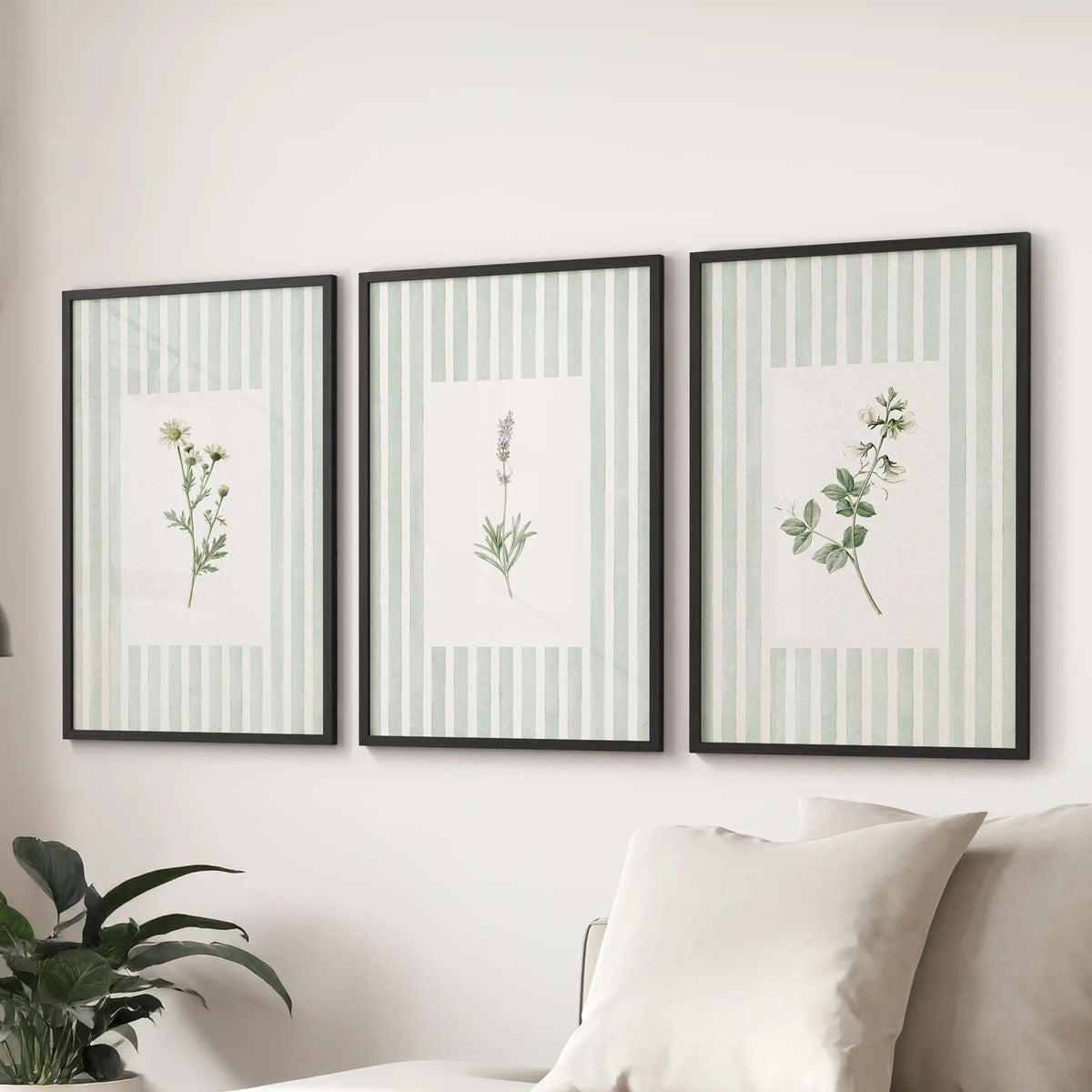 Sage botanical wall art in a three-print set is shown in black frames above a couch in a sitting room, with a different floral study in each print.