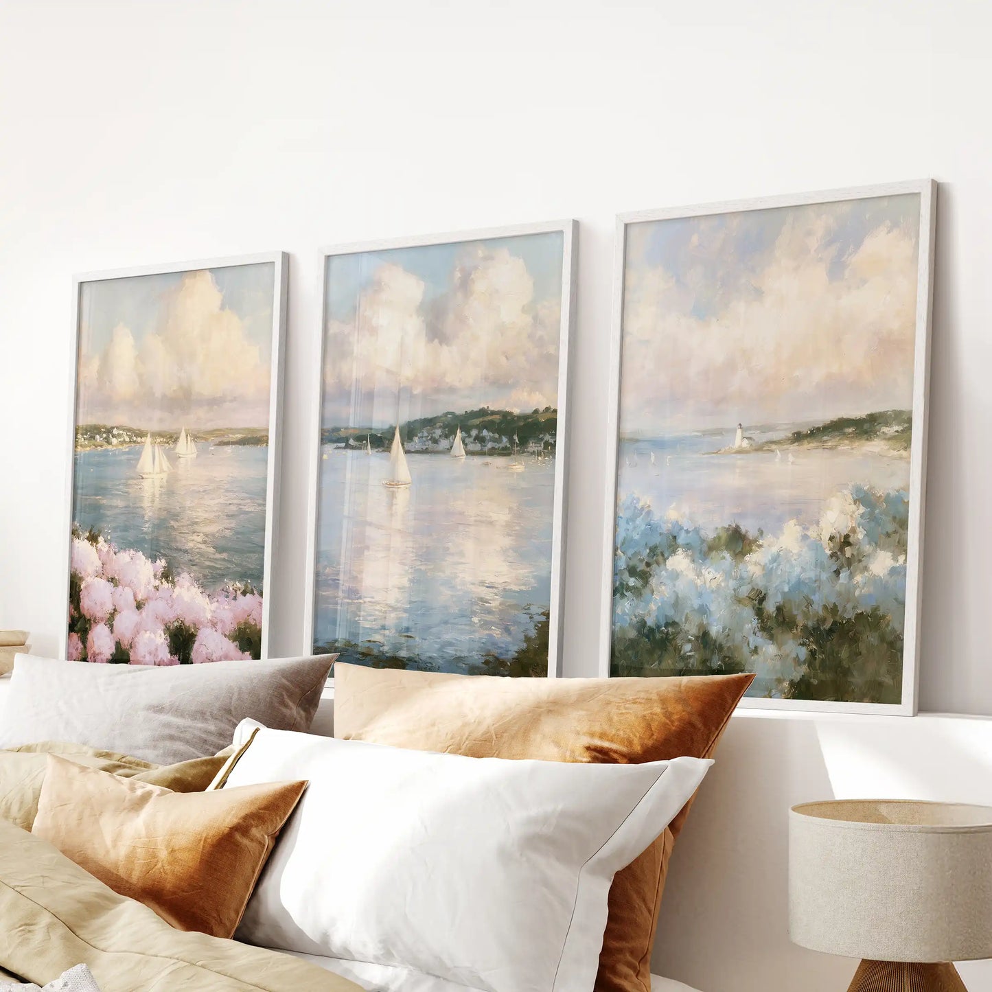 A print trio set of Nantucket sailboats tops the bedroom headboard. White frame styling gives the wall a clean nautical look with open-sky calm.