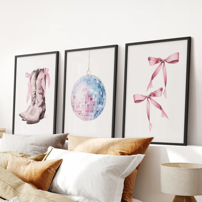 Three black-framed art prints, washed in coastal pink and blue, top a bedroom headboard and bring relaxed beach-meets-preppy charm.