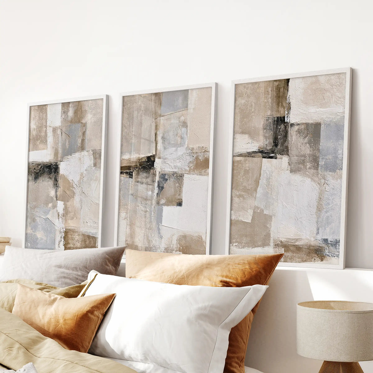 Textured beige abstracts in a set of three framed artworks bring quiet texture over the bed, their white frames suiting a serene bedroom scheme.