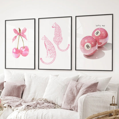 Glam pink wall decor trio cherries with bow, cheetah illustrations, and sparkling billiard 8-ball artwork. Black frames above the sofa.