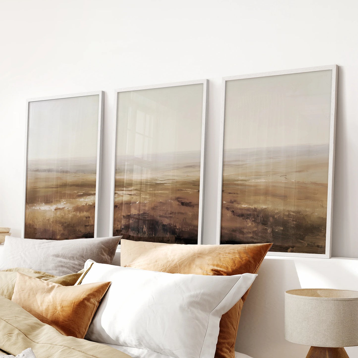 Oil painting landscape print trio makes a calm wall art focal point above the headboard in a bedroom, shown in crisp white frames.