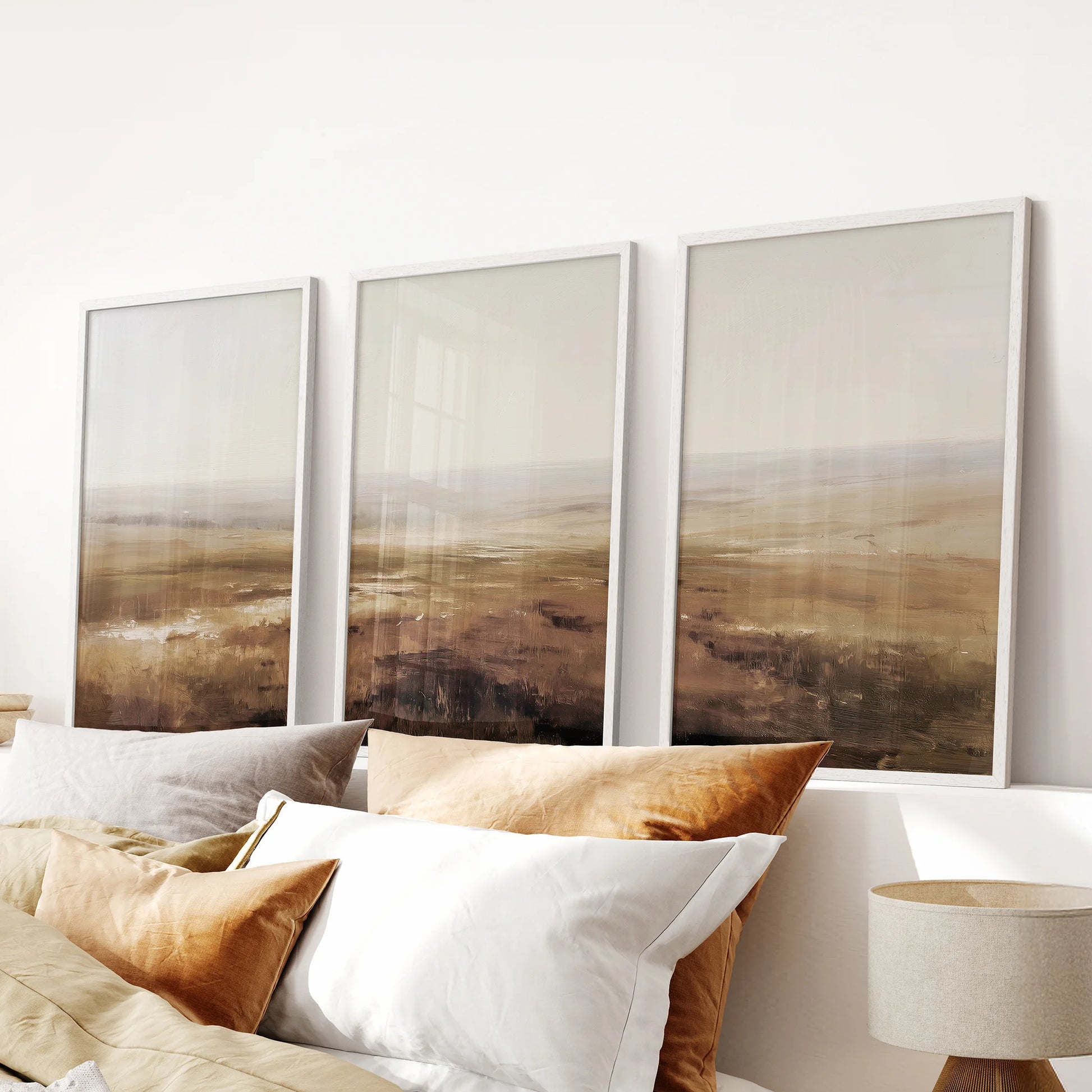 Oil painting landscape print trio makes a calm wall art focal point above the headboard in a bedroom, shown in crisp white frames.