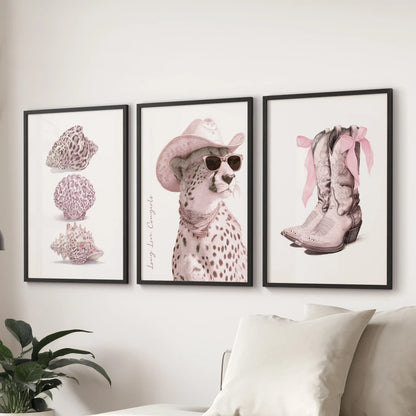 Three black-framed posters with bold lettering and pink details hang above a lounge sectional, celebrating cowgirl spirit with graphic charm.