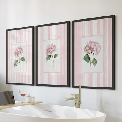 Pink striped florals in a three-piece wall decor set are displayed in black frames above a freestanding tub in a bathroom.