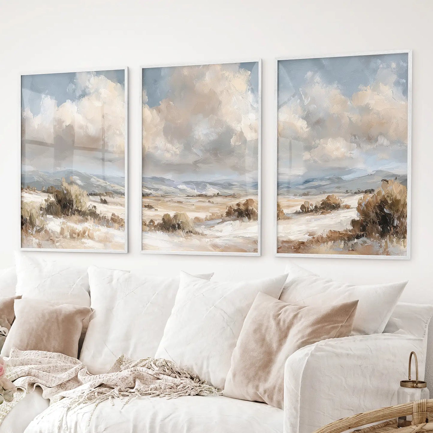 Landscape triptych in beige and blue tones. Neutral countryside prints. White frames above the sofa.