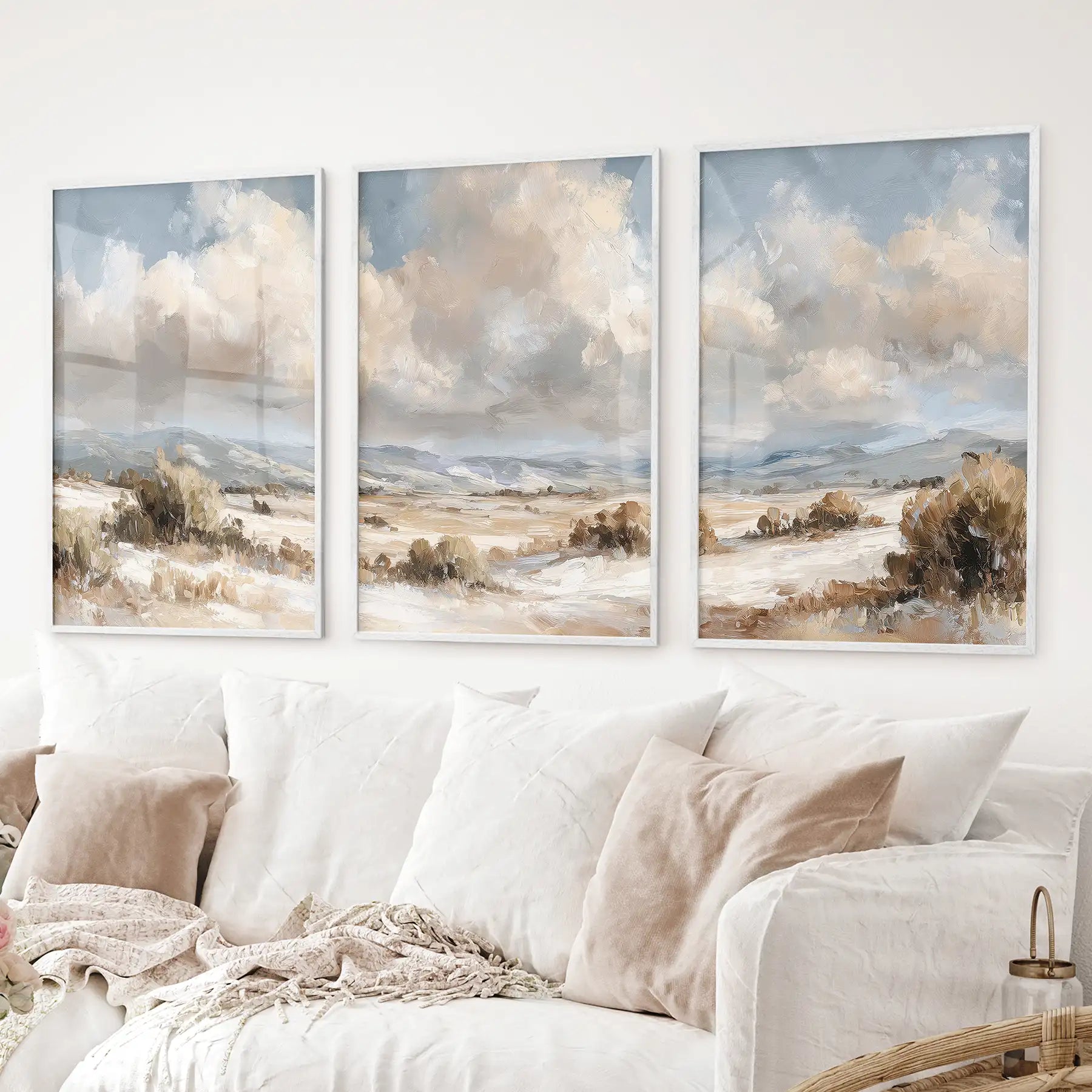 Landscape triptych in beige and blue tones. Neutral countryside prints. White frames above the sofa.