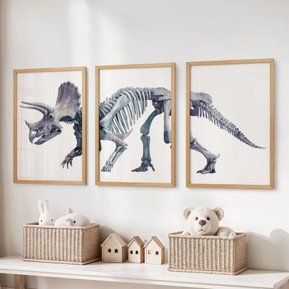Set of three watercolor triceratops skeleton posters framed in black and arranged above nursery furniture.