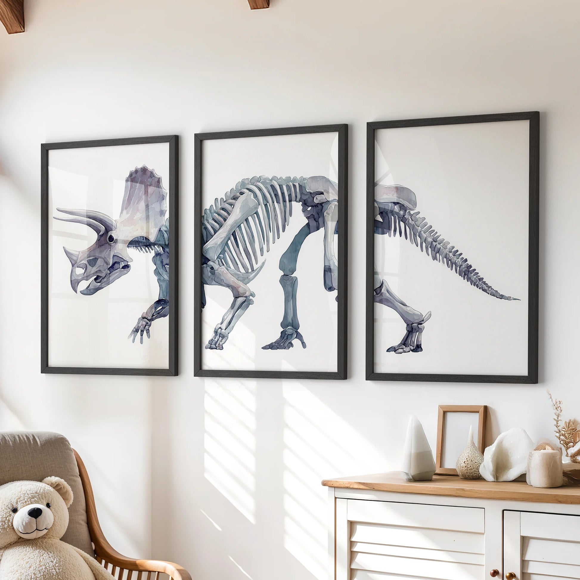Watercolor triceratops skeleton wall art set of three framed prints hanging above a wooden dresser in a cozy nursery.