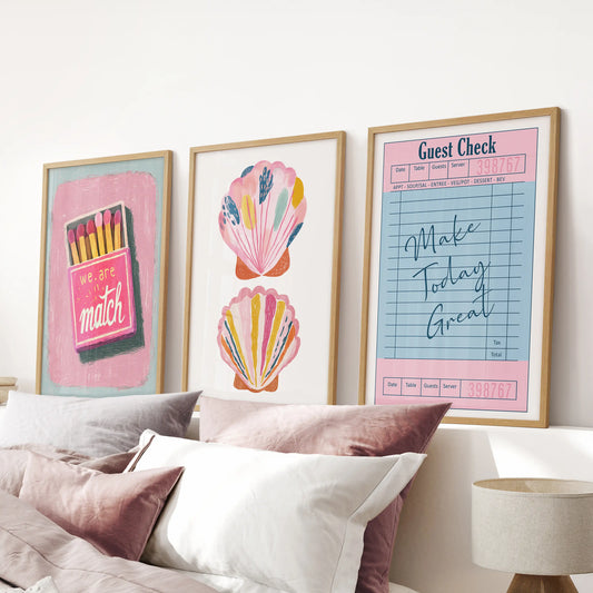 A playful trio of matchbox-style posters in warm wood frames hangs above the bed, lending the pink bedroom a retro summer charm.