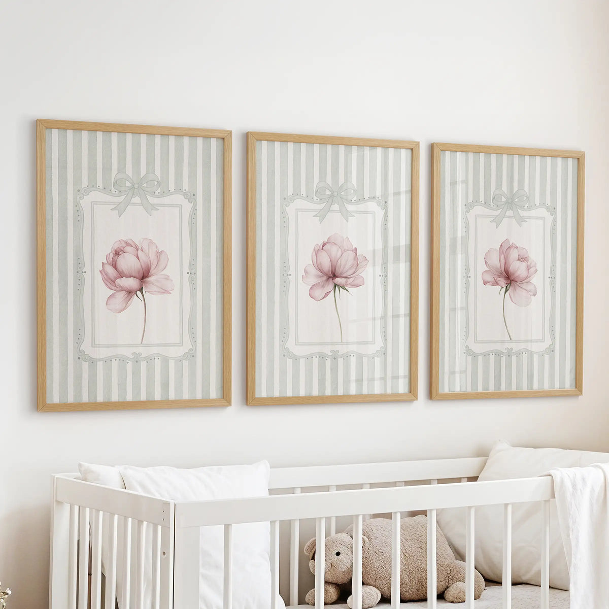 Three-piece peony botanical wall art set in oak frames, with pink flowers on sage green stripes displayed over a crib.