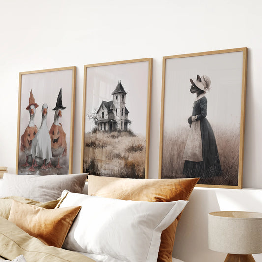 A three-print haunted house and ghost set in light oak frames centers over the bed headboard, layering subtle Halloween spirit in the bedroom.