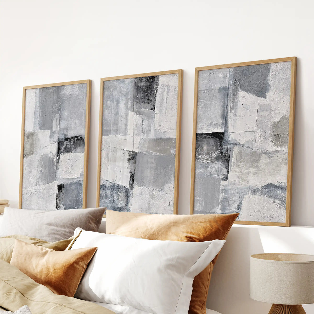 A three-print wall art bundle of soft gray brushstroke studies, framed in natural oak, anchors the space above the bed with hushed movement.