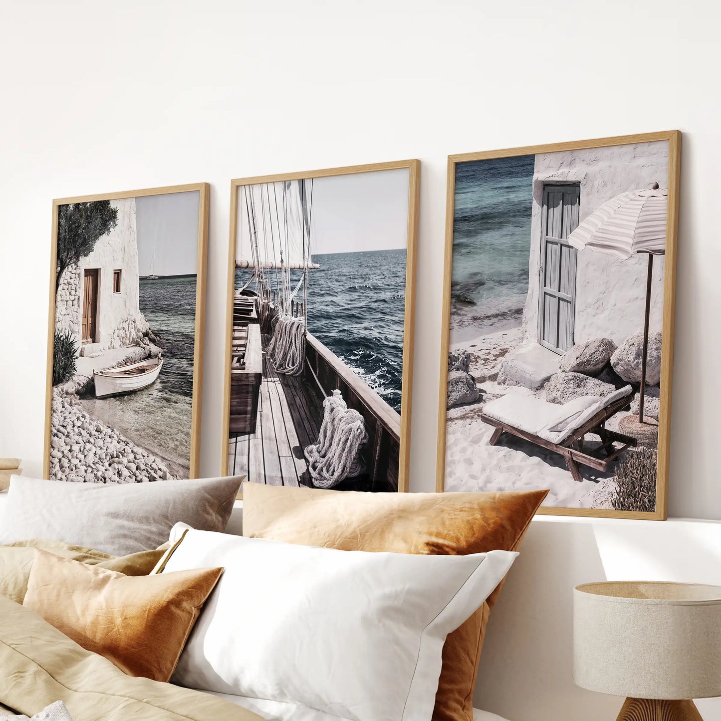 A three-piece wall decor set shows Mediterranean sailboats in oak-framed prints, placed above the bed headboard as a calm, breezy bedroom focal point.