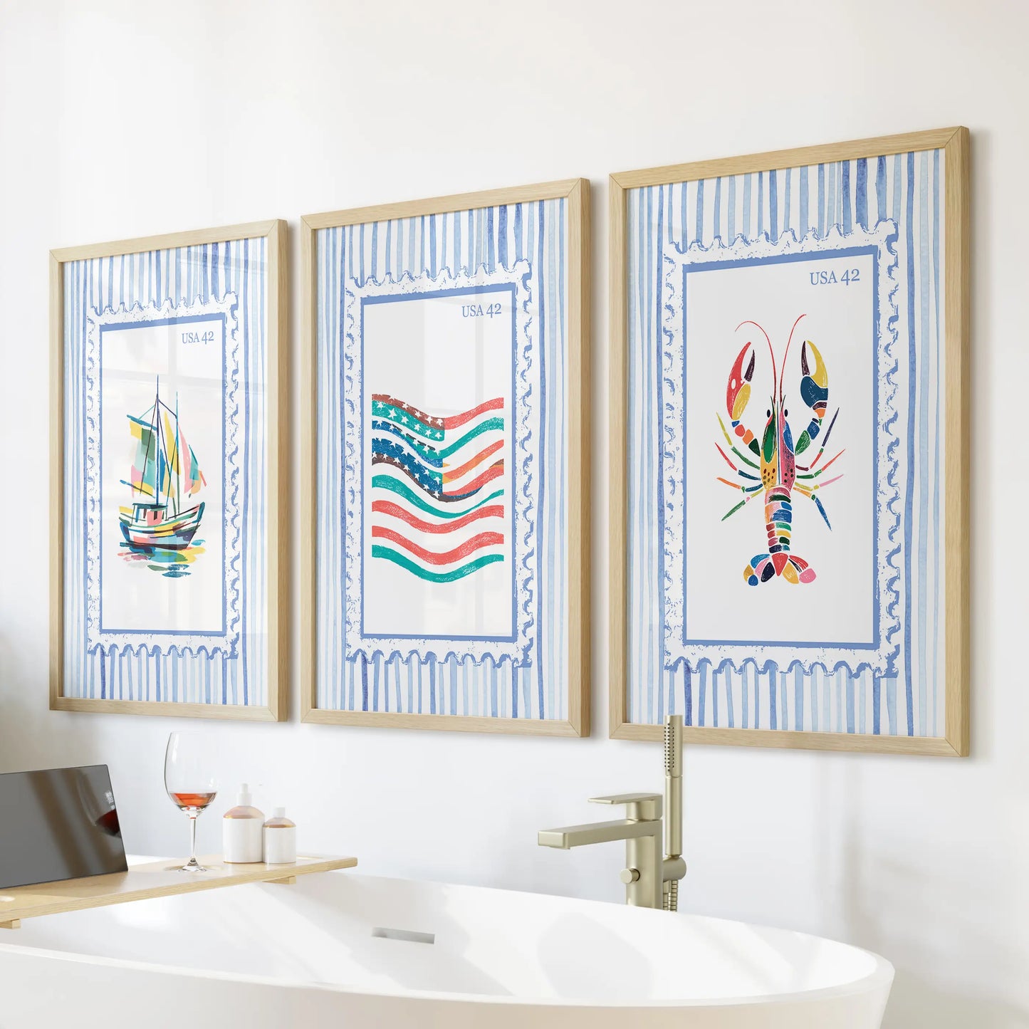 Three beach stamp prints in slim wood frames form a light gallery wall above the freestanding tub for an easy lake-house feel.