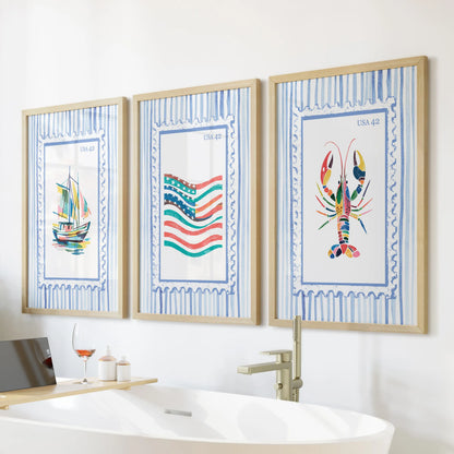 Three beach stamp prints in slim wood frames form a light gallery wall above the freestanding tub for an easy lake-house feel.
