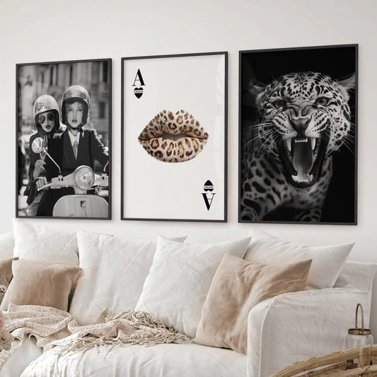 Glam wall art triptych with leopard, lips playing card, and stylish scooter poster. Black frames over the couch.