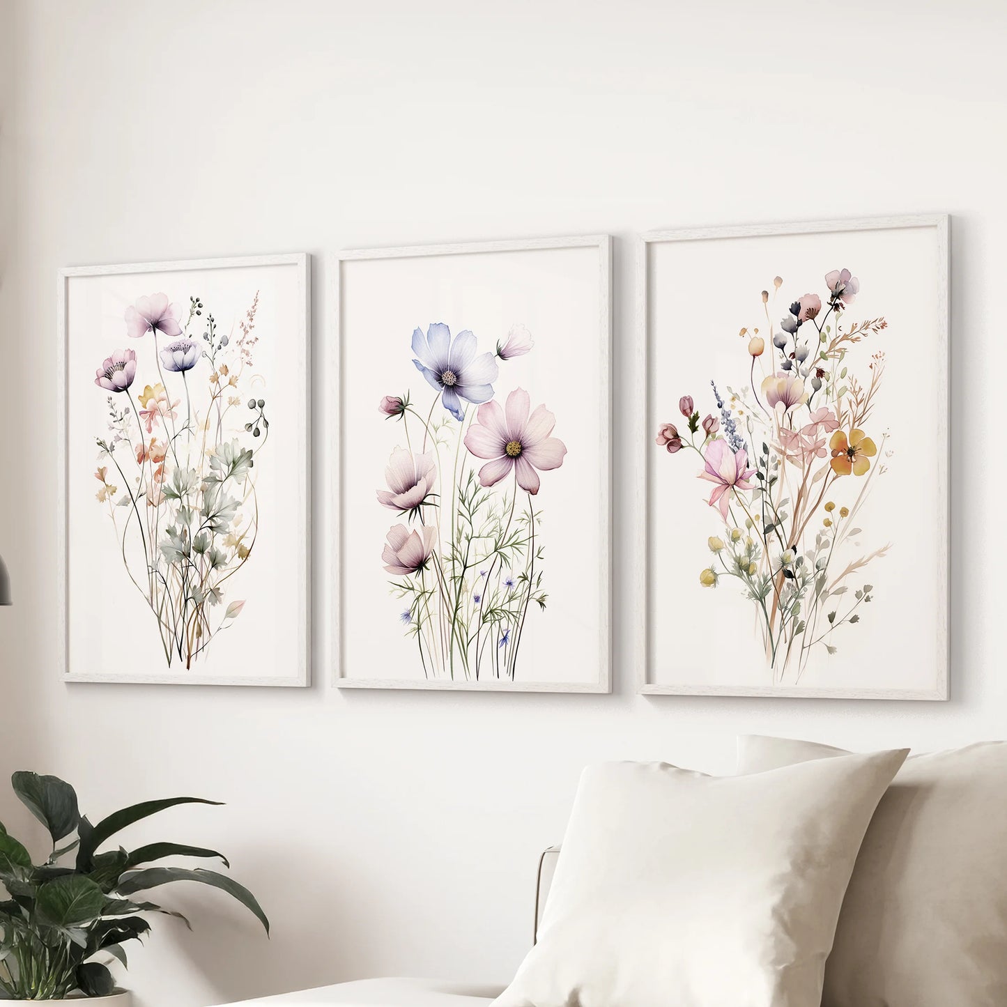 Three watercolor wildflower paintings framed in white form a bright wall art trio, styling the living room gracefully over the couch.