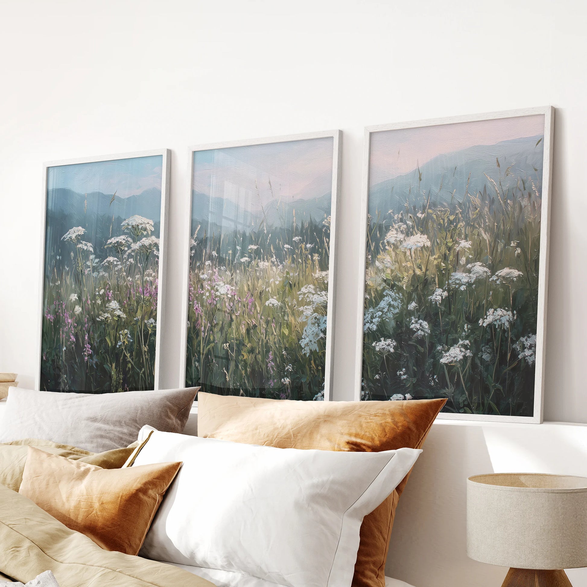 White-framed landscape posters in a 3-piece set create an airy farmhouse accent above the bed headboard in a serene bedroom.