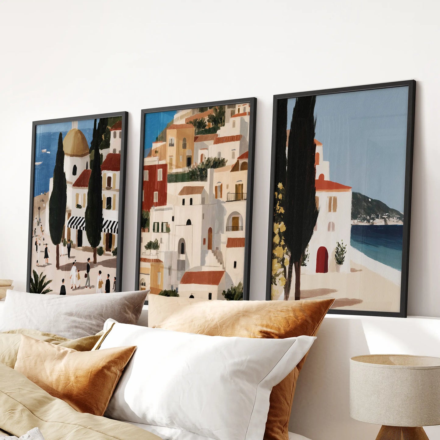 Three Spanish seaside village prints in black frames hang neatly above the bed, centering a bedroom with an easy coastal feel.