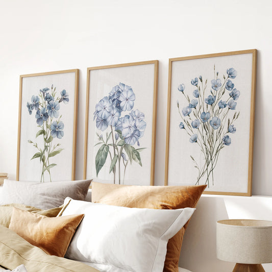 A set of three watercolor botanical artworks in thin wood frames settles over the headboard, adding soft blue hydrangeas to the bedroom wall.