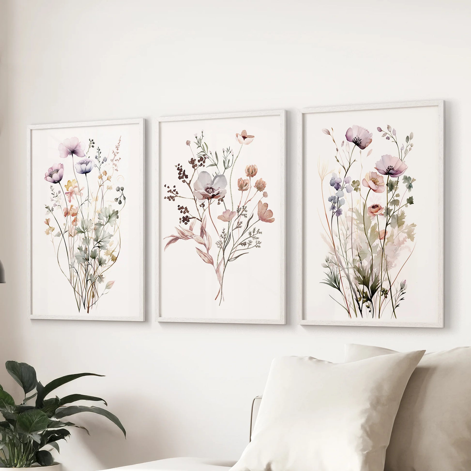 Three watercolor wildflower posters in white frames arranged above a sectional sofa, grounding the living room with gentle nature-inspired color.
