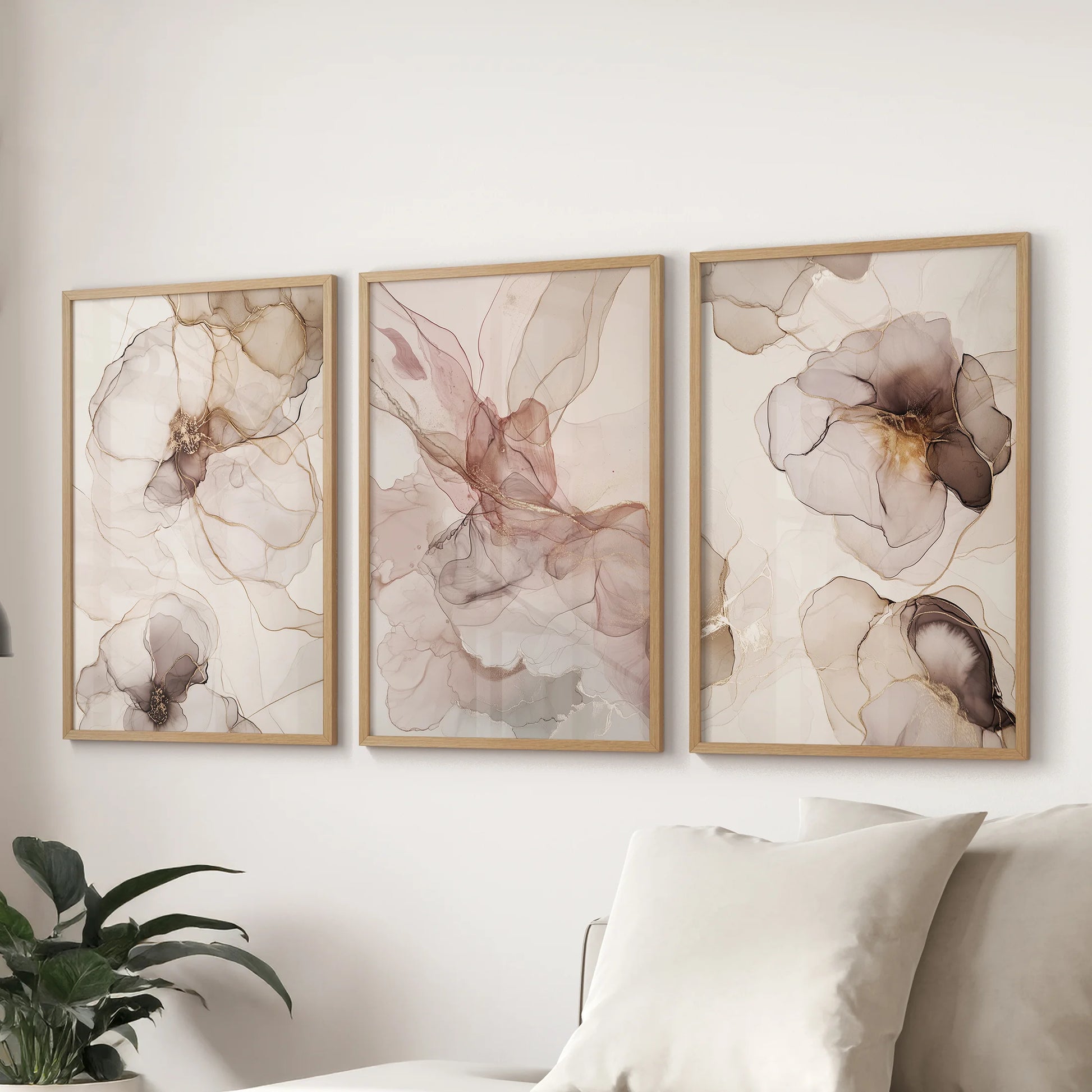 A set of three artwork prints in natural wood frames shows blush and beige abstractions, giving the lounge a gentle modern look over the couch.
