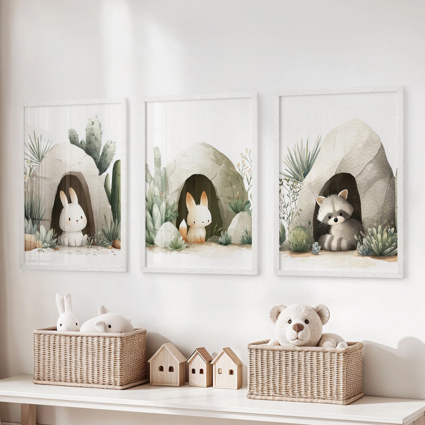 Three white-framed nursery prints—two bunnies and a raccoon in cave scenes with sage plants—above wicker baskets and toys.