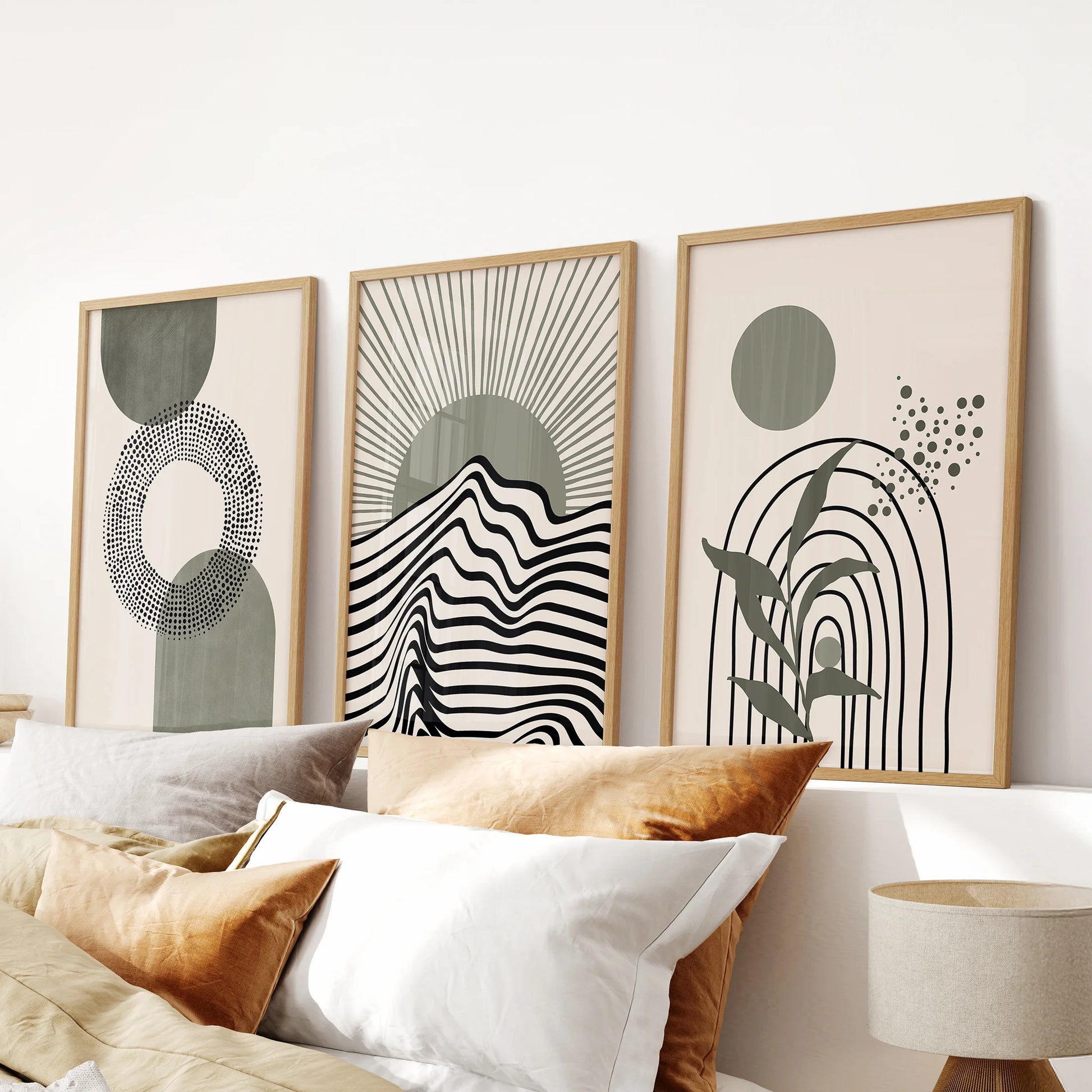 Modern boho sage designs set of 3 pictures hangs over the bed in a calm bedroom, oak framed for warmth and a subtly mid-century, botanical feel.