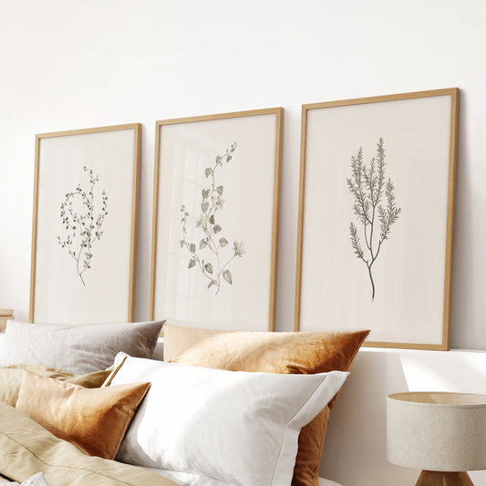 Neutral cottagecore botanicals, a three-piece picture set in natural wood frames, sits above the bed's headboard to ground the bedroom with subtle warmth.