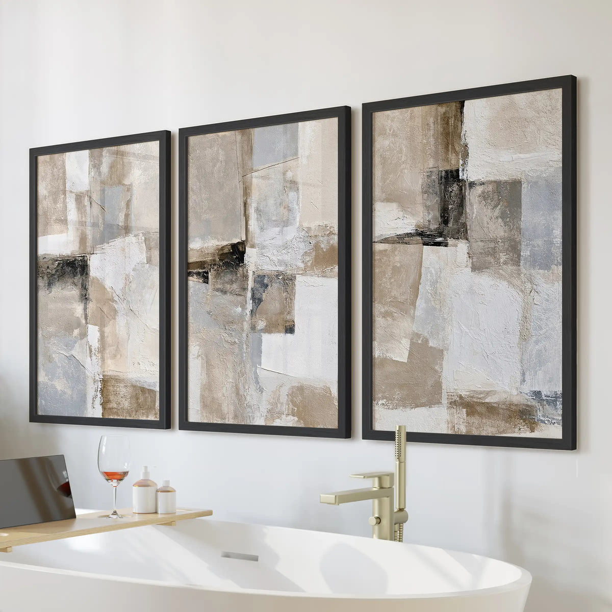 Textured beige abstracts, a three-piece wall art set, hangs over the soaking tub in a modern bathroom, finished in sleek black frames.